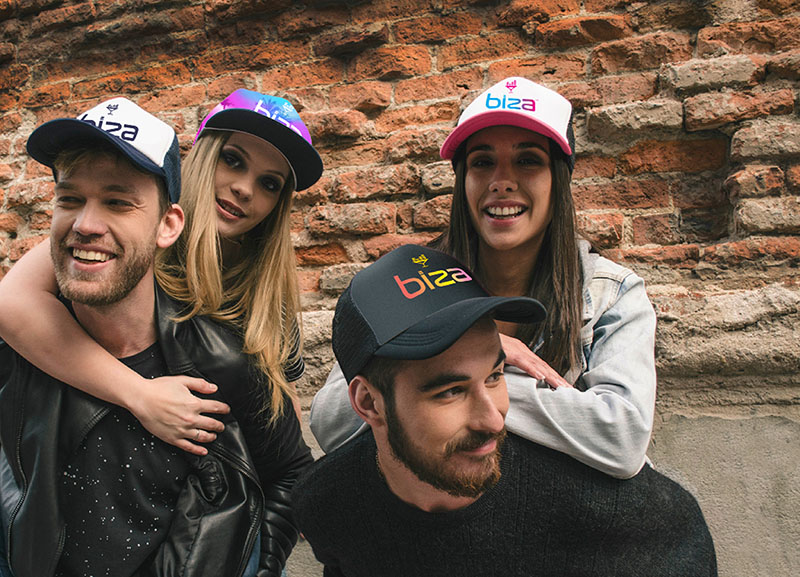 Four friends smiling and hanging out next to a brick wall with Biza hats on.