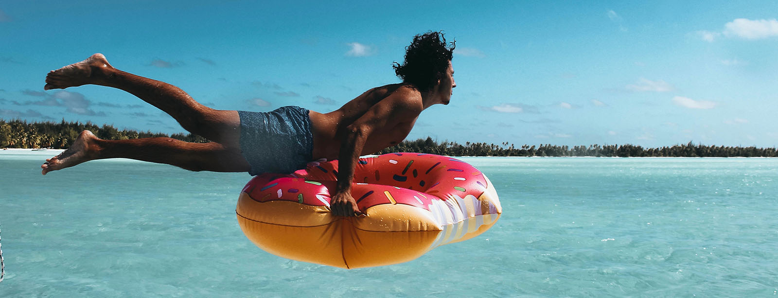 Guy jumping into the ocean with a donut inner tube.